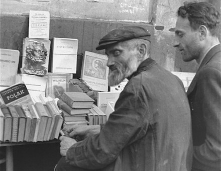 Book vendors sit in front of a table piled with books on a street in the Warsaw ghetto., c. June-August 1941. United States Holocaust Memorial Museum, courtesy of Rafael Scharf.